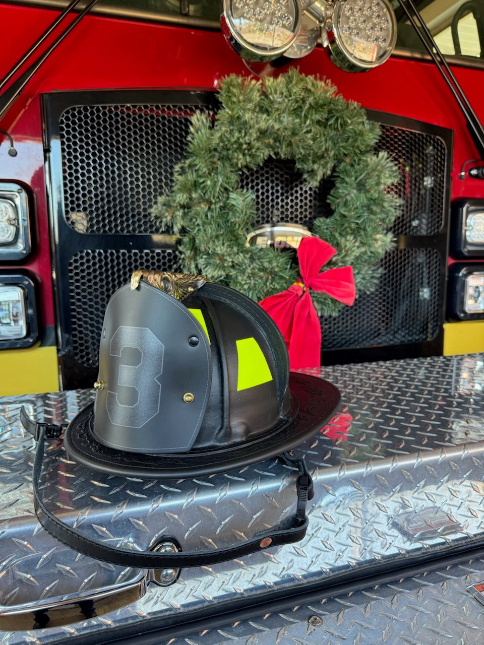 Box 31 Boston-style shield in "blackout" color scheme, sitting on the front bumper of a red fire engine with a green Christmas wreath