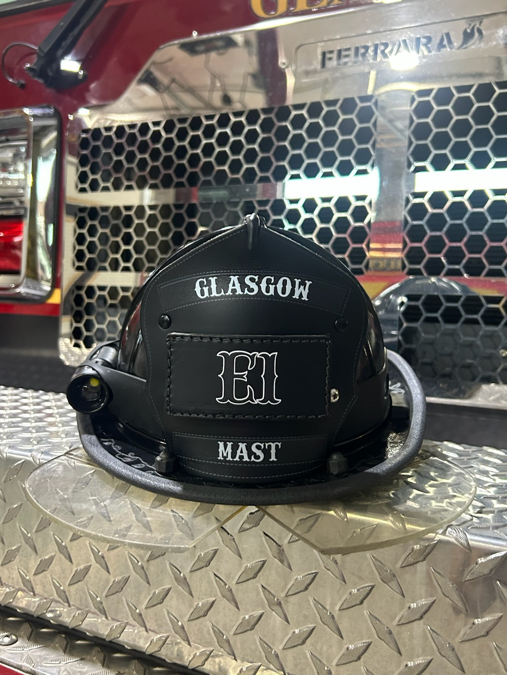 This black and white Box 31 passport shield is in service in Glasgow, KY. Shield is shown on a black helmet, sitting on the front bumper of a Ferrara fire engine.