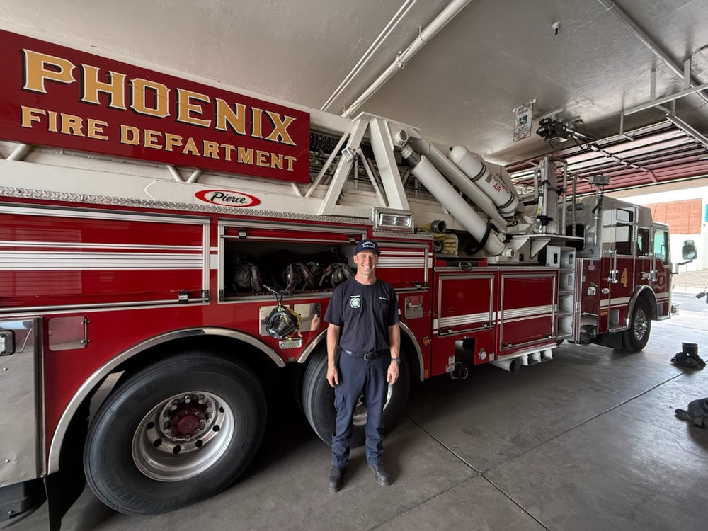 A smiling firefighter stands in front of Phoenix Ladder 4 with a Box 31 SCBA Quick Release hanging from an airpack in the side compartment.