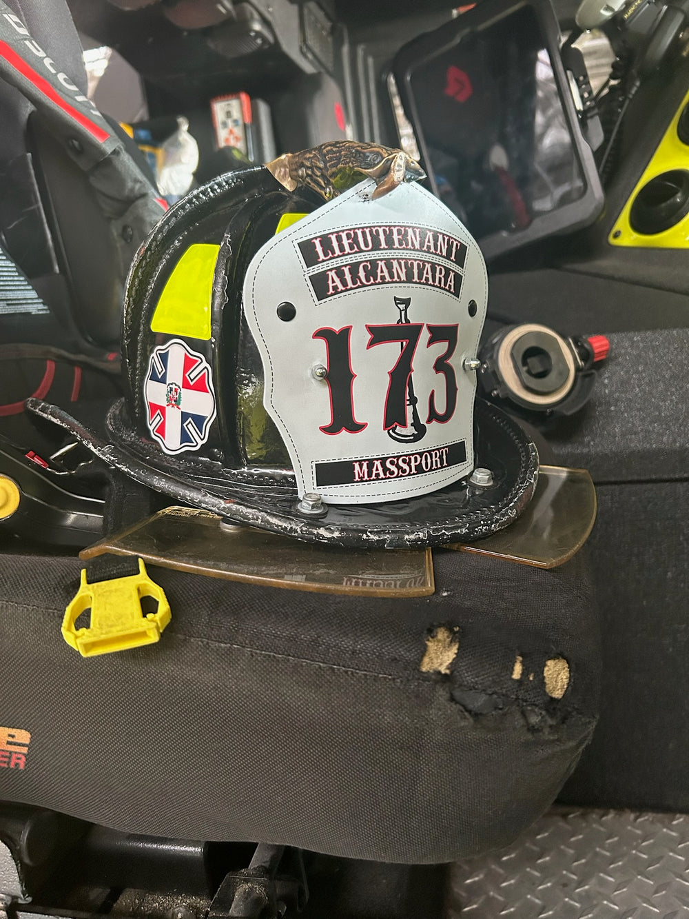 This in service white traditional helmet shield is printed in Box 31's 2-1 text and bugles style, with two lines of text at the top, one line at the bottom, and large numbers in the middle with a single silver bugle behind the numbers. Shown on a black helmet sitting in the officer's seat of an engine in Massachusetts.