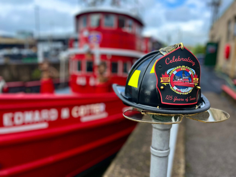 Custom Box 31 shield celebrates 125 years of service for the Edward M. Cotter fire boat in Buffalo, NY. Shield is installed on a helmet and sitting on a stanchion with the boat in the background.