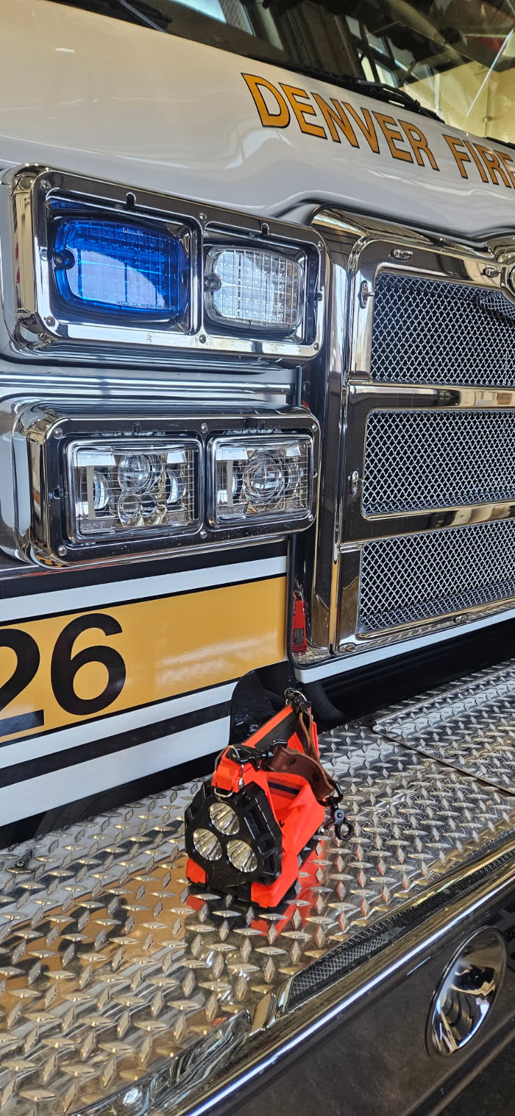 An orange box light with a Box 31 medium brown leather Box Light Clip sits on the front bumper of a yellow and white Denver Fire Department engine.